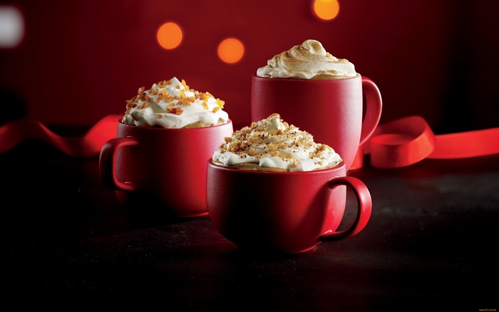 Three red coffee cups with whipped cream and toppings