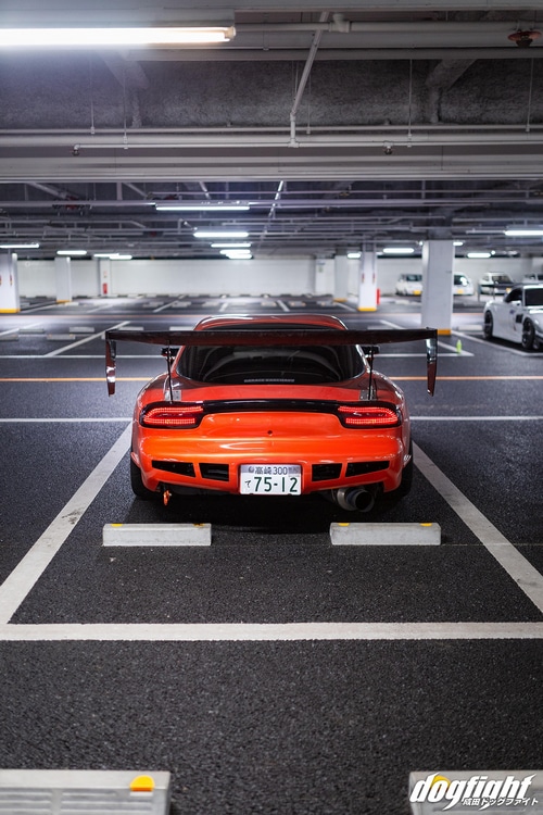 Orange Mazda RX-7 with large rear wing in parking garage