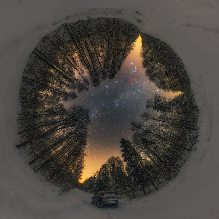Winter night sky over a snowy forest with a car