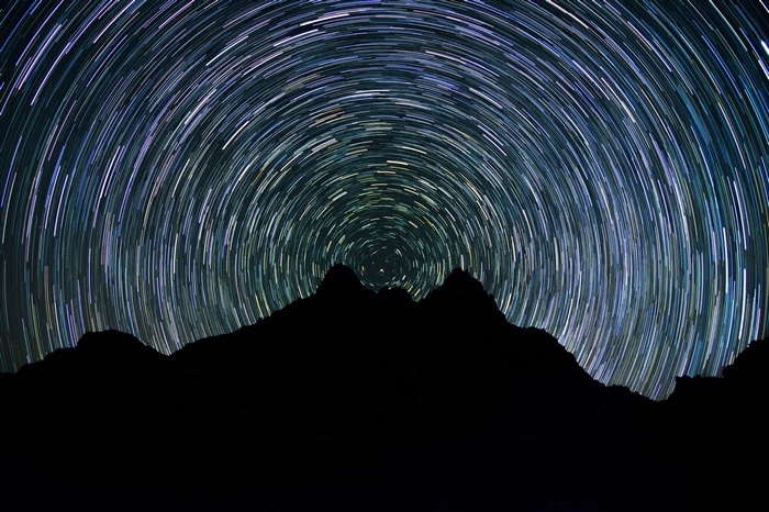 Star trails over silhouetted mountains at night