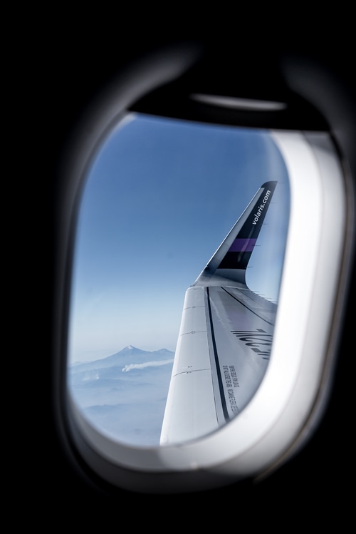 Airplane wing with Volaris logo flying over mountains