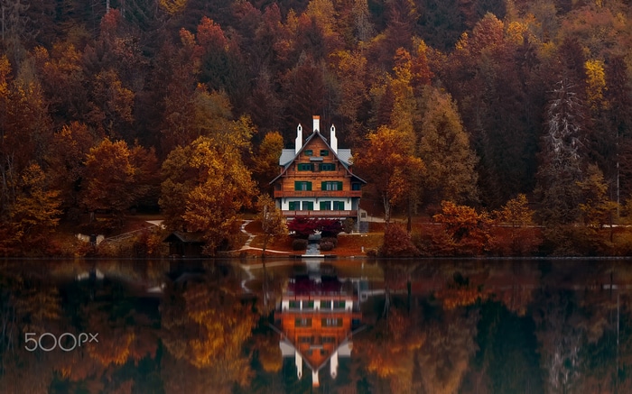 Wooden house reflected in a lake surrounded by autumn forest