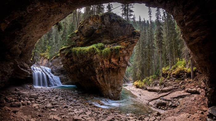 Cave entrance with waterfall and rock formation in forest