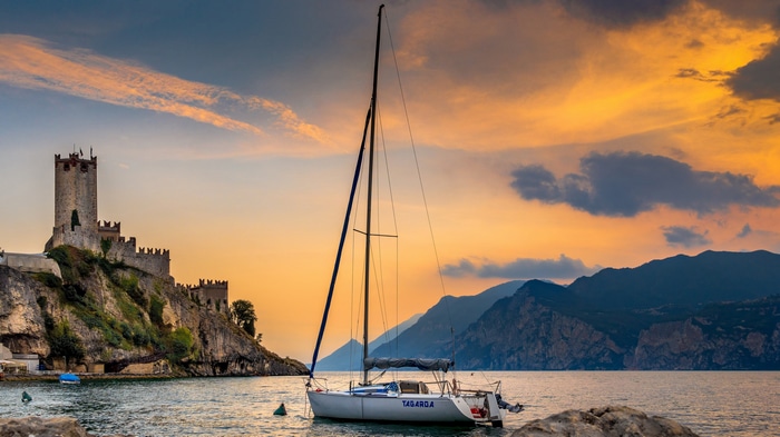 Castle and sailboat on Lake Garda at sunset