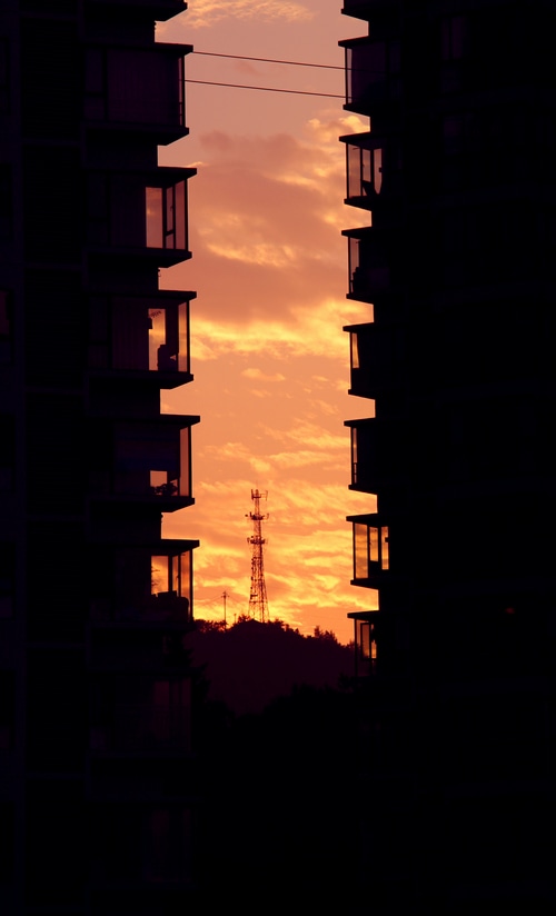 Apartment buildings framing a sunset with a cell tower