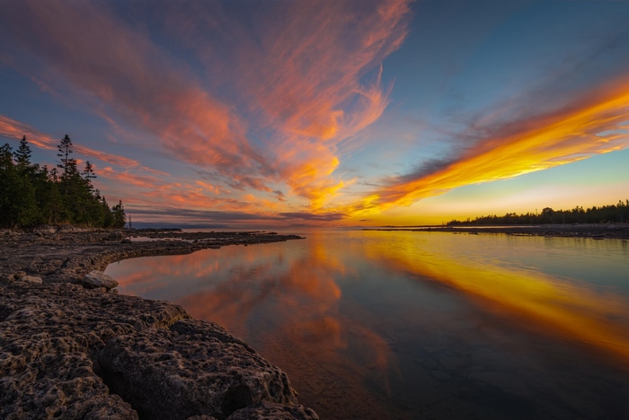 Sunset over a rocky shore with colorful clouds and reflection