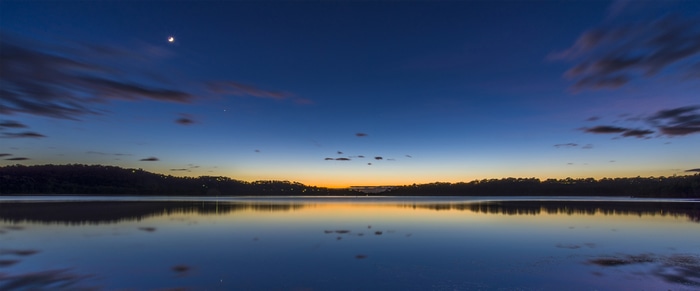 Calm lake at dusk with moon and clouds
