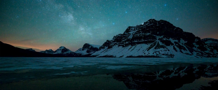 Snowy mountains under a starry night sky with reflection