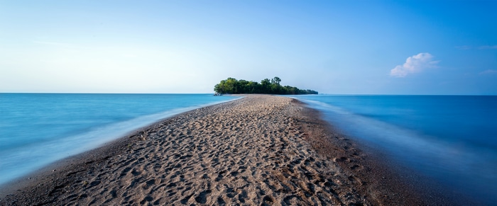 4K sand spit leading to a tree-covered island