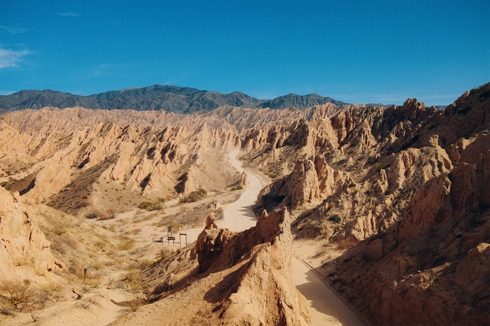 Winding dirt road through a desert canyon with mountains in the background