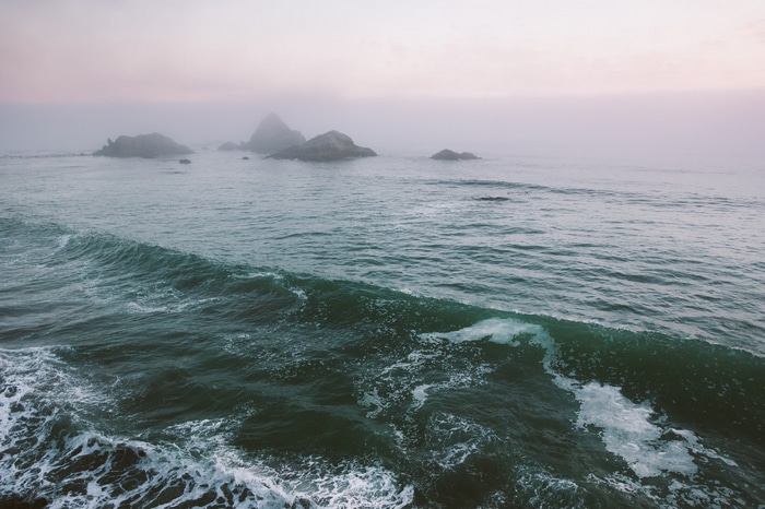 Ocean waves crashing near rocky islands in the fog