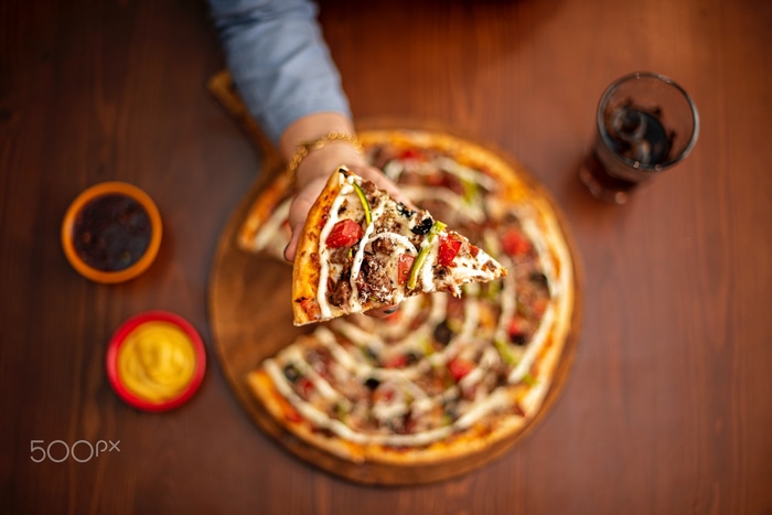 Slice of pizza being held over a whole pizza