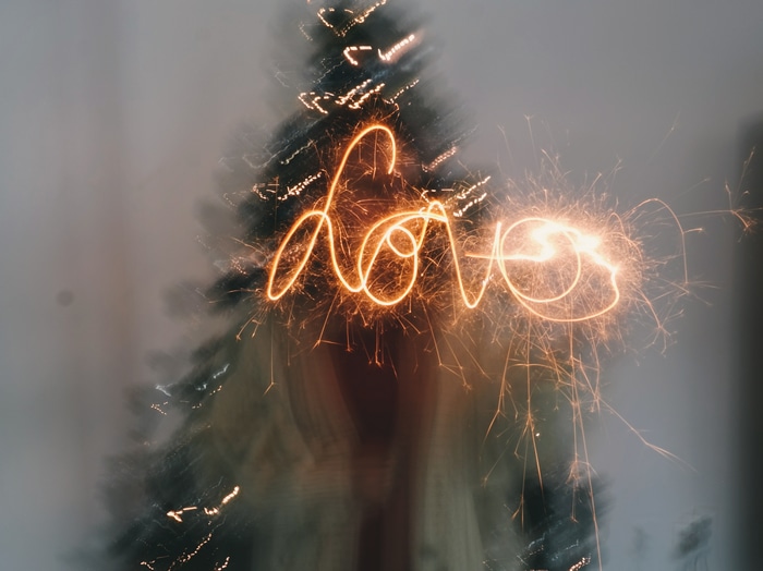 Love written in sparklers with Christmas tree background