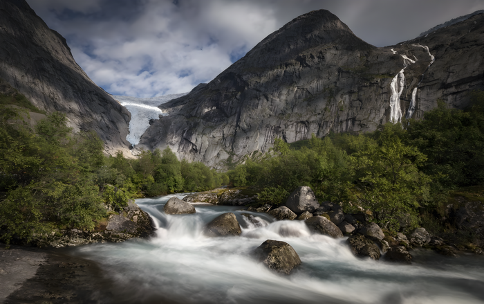 Glacier and river flowing through mountains with trees