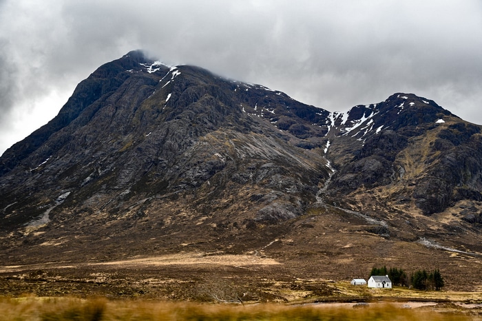 A lone white house sits at the base of a rugged mountain.