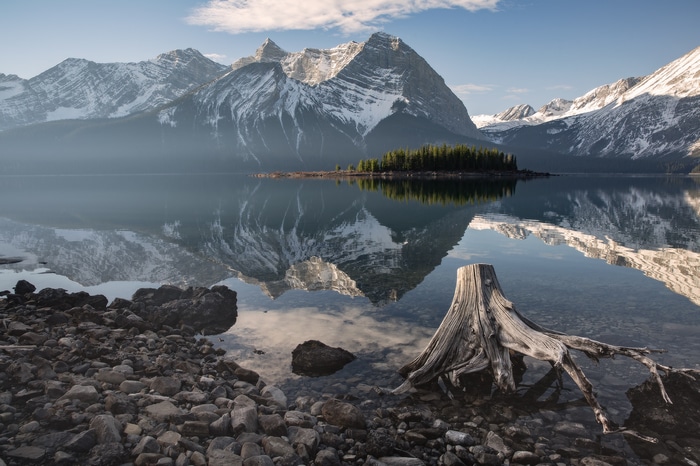 Snowy mountains reflected in a calm lake with a tree stump