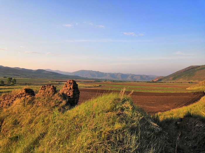 Landscape with fields, rocks, and mountains under a blue sky