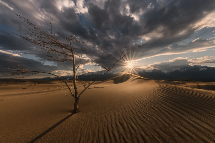 Sunset over sand dunes with mountains and clouds