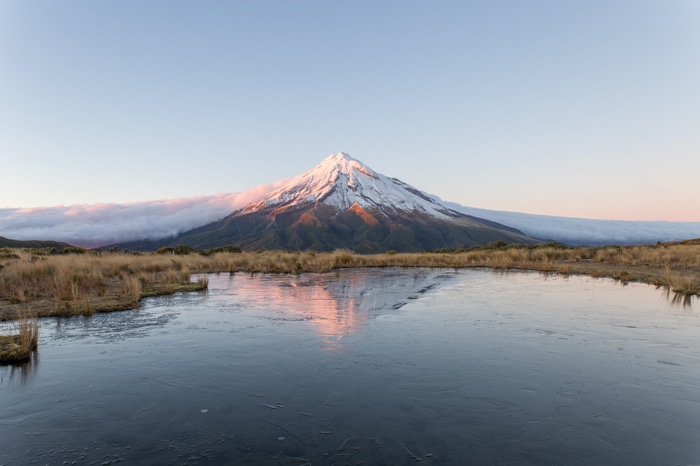 Mount Taranaki reflected in a frozen pond at sunrise