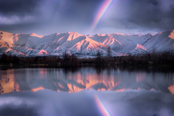 Snow-capped mountains reflected in a lake with a rainbow