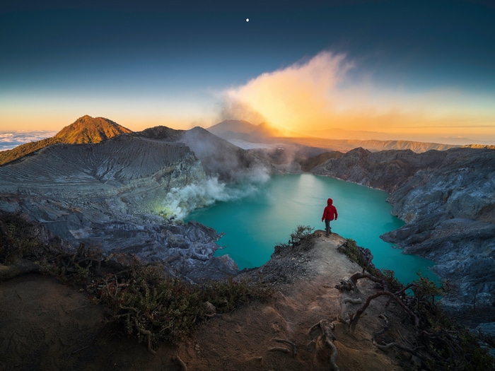 Mount Ijen crater lake at sunrise with a lone hiker