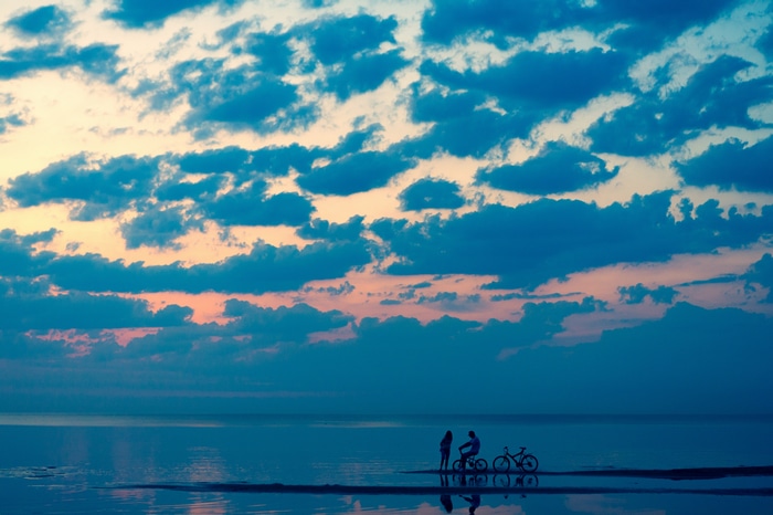 Couple with bicycles on a beach at sunset