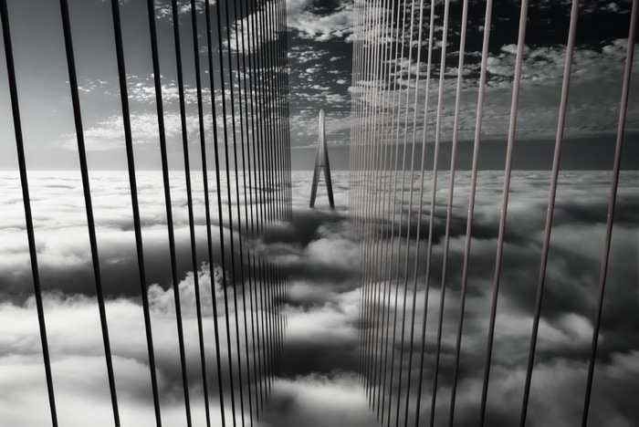 Monochrome suspension bridge above clouds
