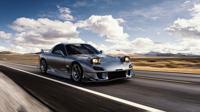 Silver Mazda RX-7 driving on a road with mountains