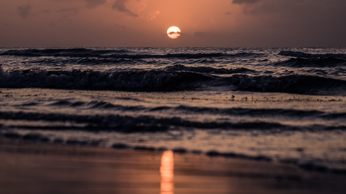 Sunset over the ocean with waves crashing on the shore