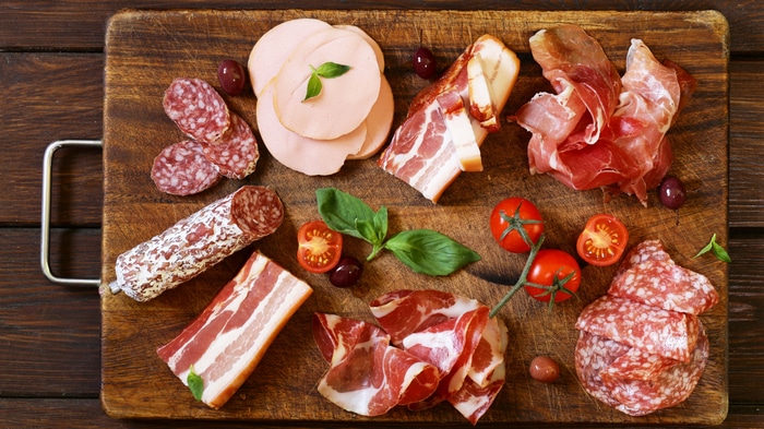 Assortment of cured meats and tomatoes on a wooden board