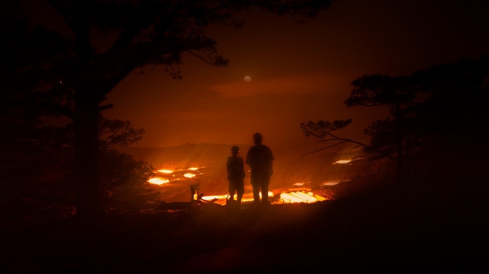 Two people watch a volcanic eruption at night