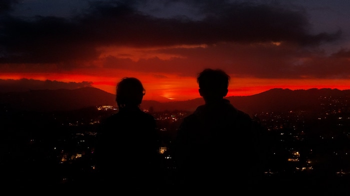 Two silhouettes watch a fiery sunset over a city