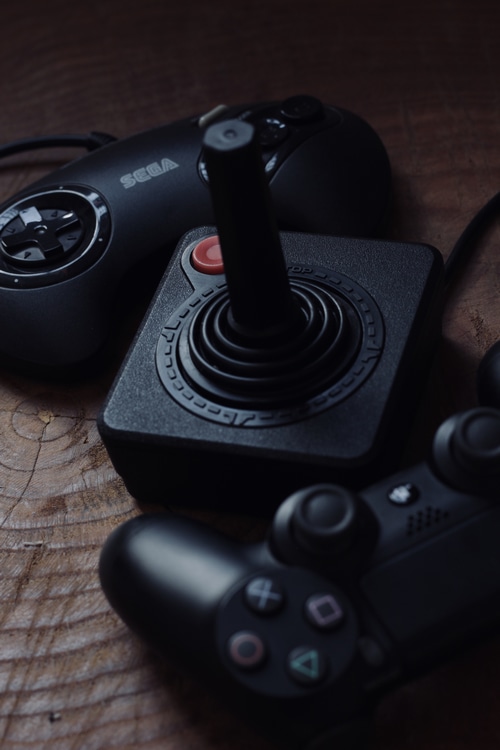 Sega, Atari, and PlayStation controllers on wood