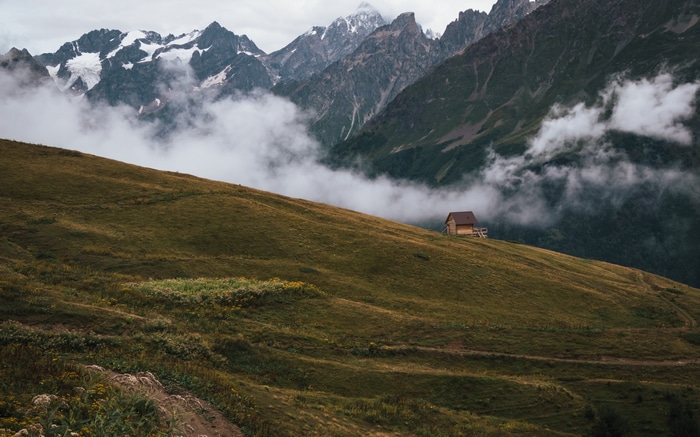4K mountains with clouds and a small cabin