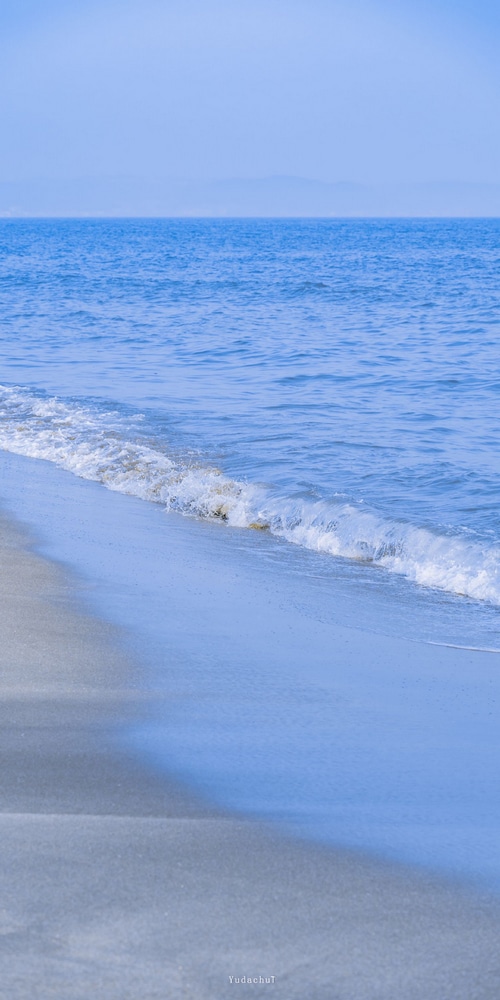 Gentle waves lap onto a sandy beach under a clear sky.