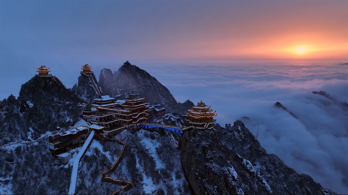 Temple on snowy mountains above clouds at sunset in China