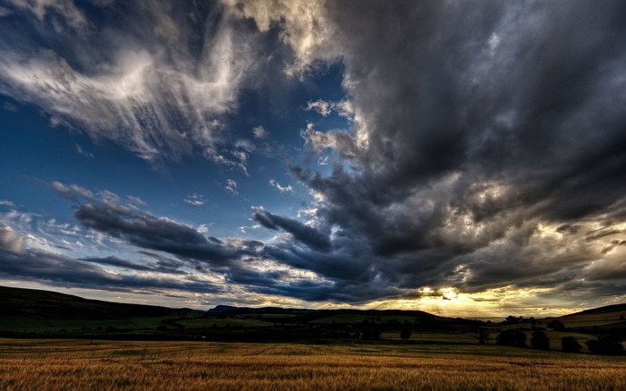 Dramatic clouds over a golden field and rolling hills
