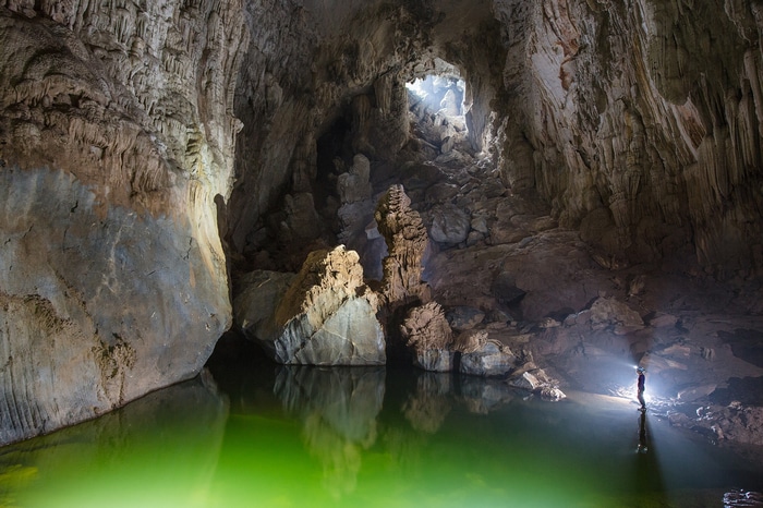 Hang Son Doong cave with green water and a person with a flashlight