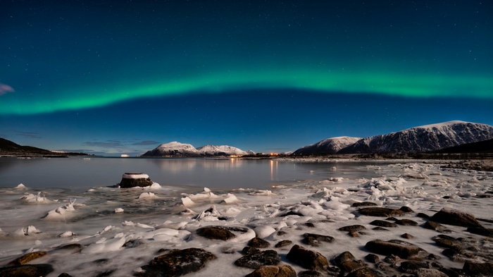 Aurora Borealis over snowy mountains and icy coast in Norway