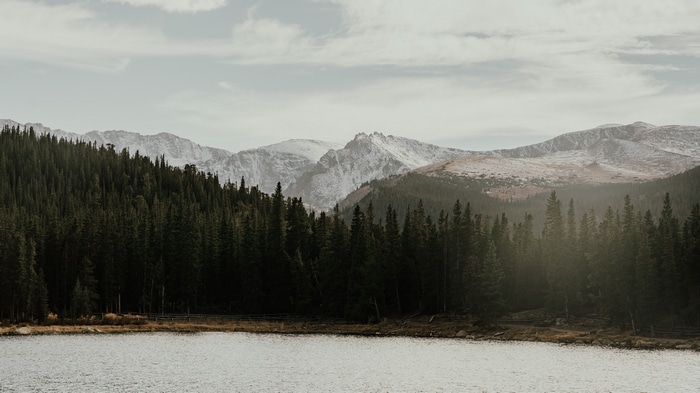 4K snow-capped mountains behind a dark forest and lake