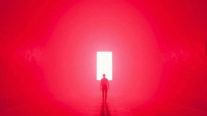 A person walks towards a bright light in a red room