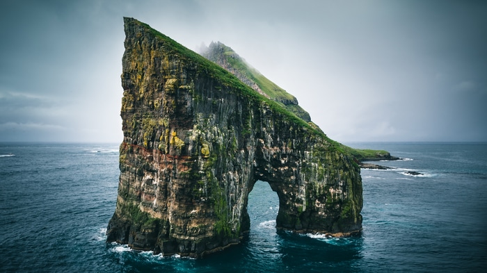 4K rock arch in the sea under a cloudy sky