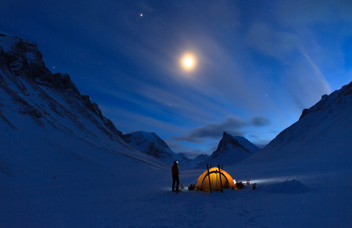 Tent in snowy mountains under moonlight