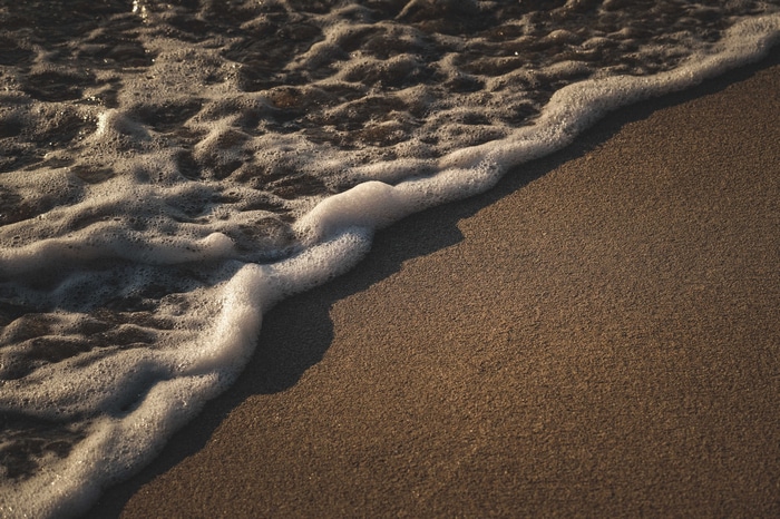 4K sea foam washing onto a sandy beach