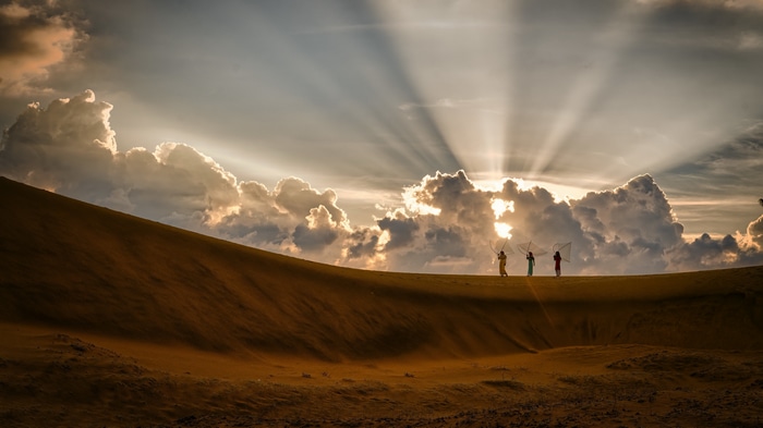 Four women with fishing nets on a sand dune at sunset
