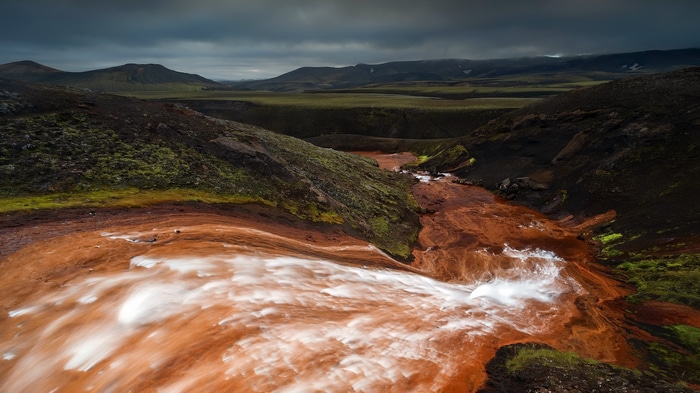 Red river flowing through a volcanic landscape under a cloudy sky