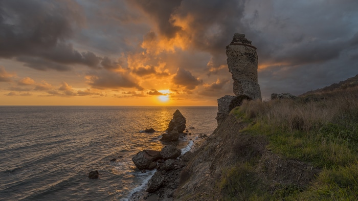 Sunset over the sea with rocks and ruins