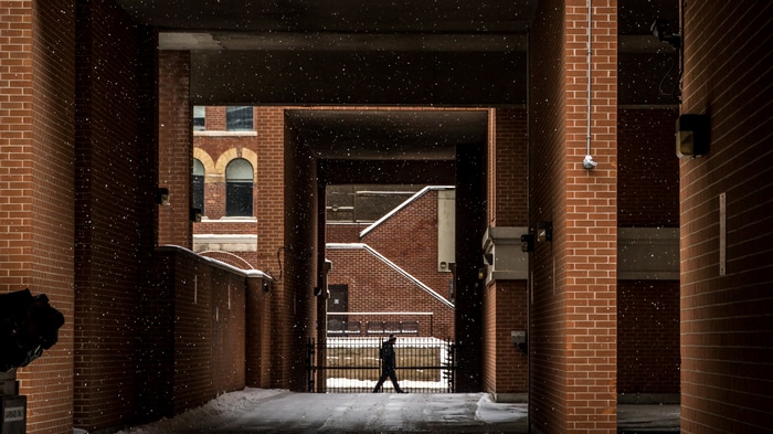 Person walking in snow between brick buildings