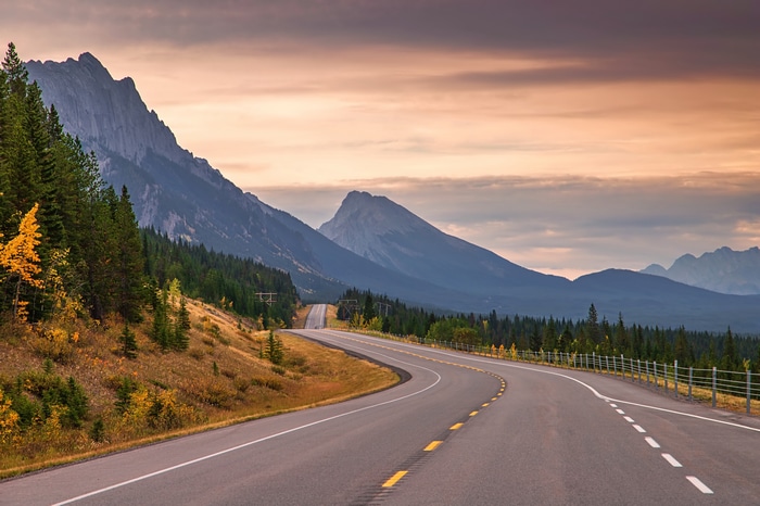 Road through mountains and forest at sunset