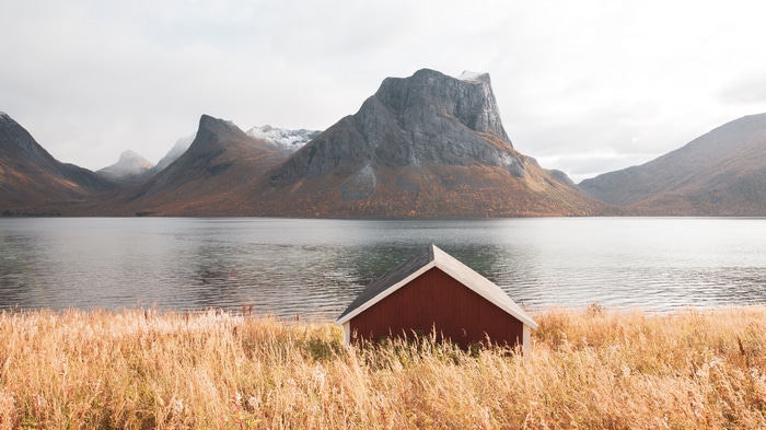 Red cabin by a lake with mountains in Norway